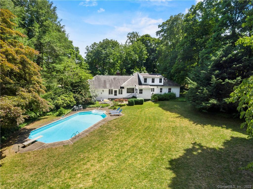 Aerial view of a white house with a backyard pool, broad lawn, and mature trees.