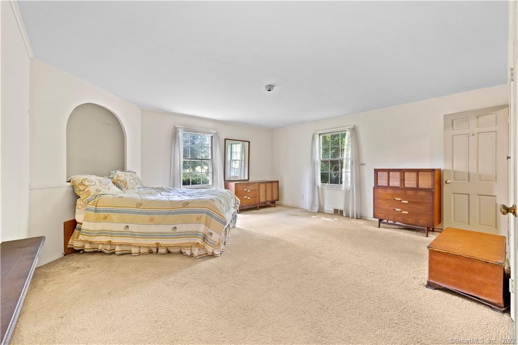 Furnished bedroom with a bed beneath an arched niche and wooden dressers.