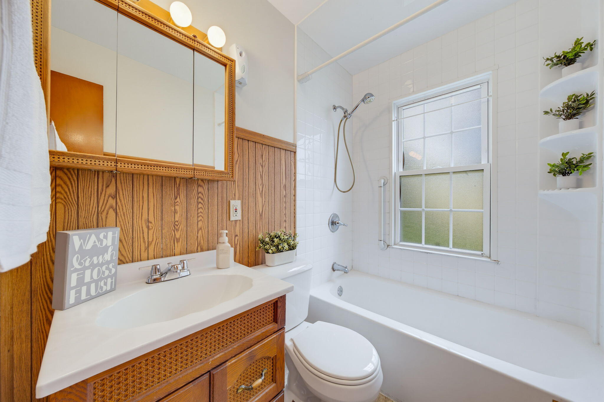 Bathroom with wood-paneled vanity, woven-front cabinets, and a white tub beneath a frosted window.
