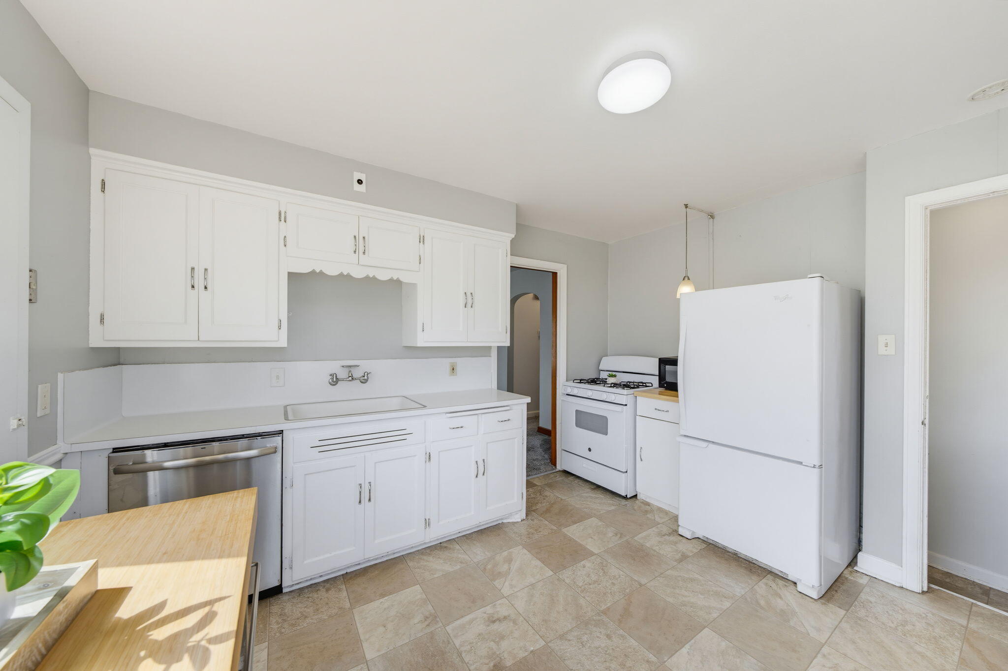Vacant kitchen with white cabinets, a gas range, refrigerator, and beige tile floor.