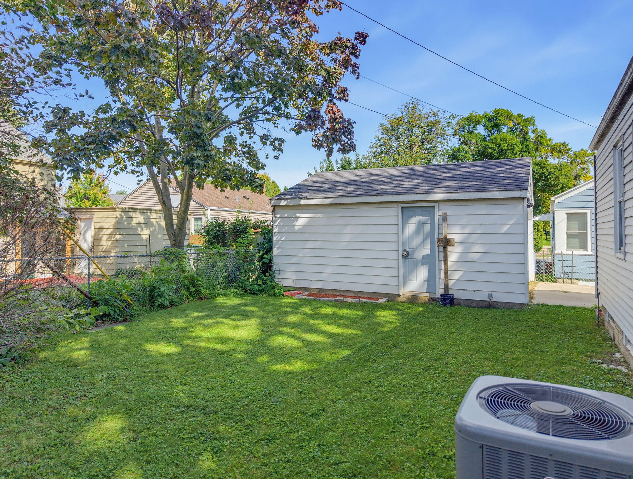 Backyard lawn with a detached garage, mature trees, and an outdoor air-conditioning unit.