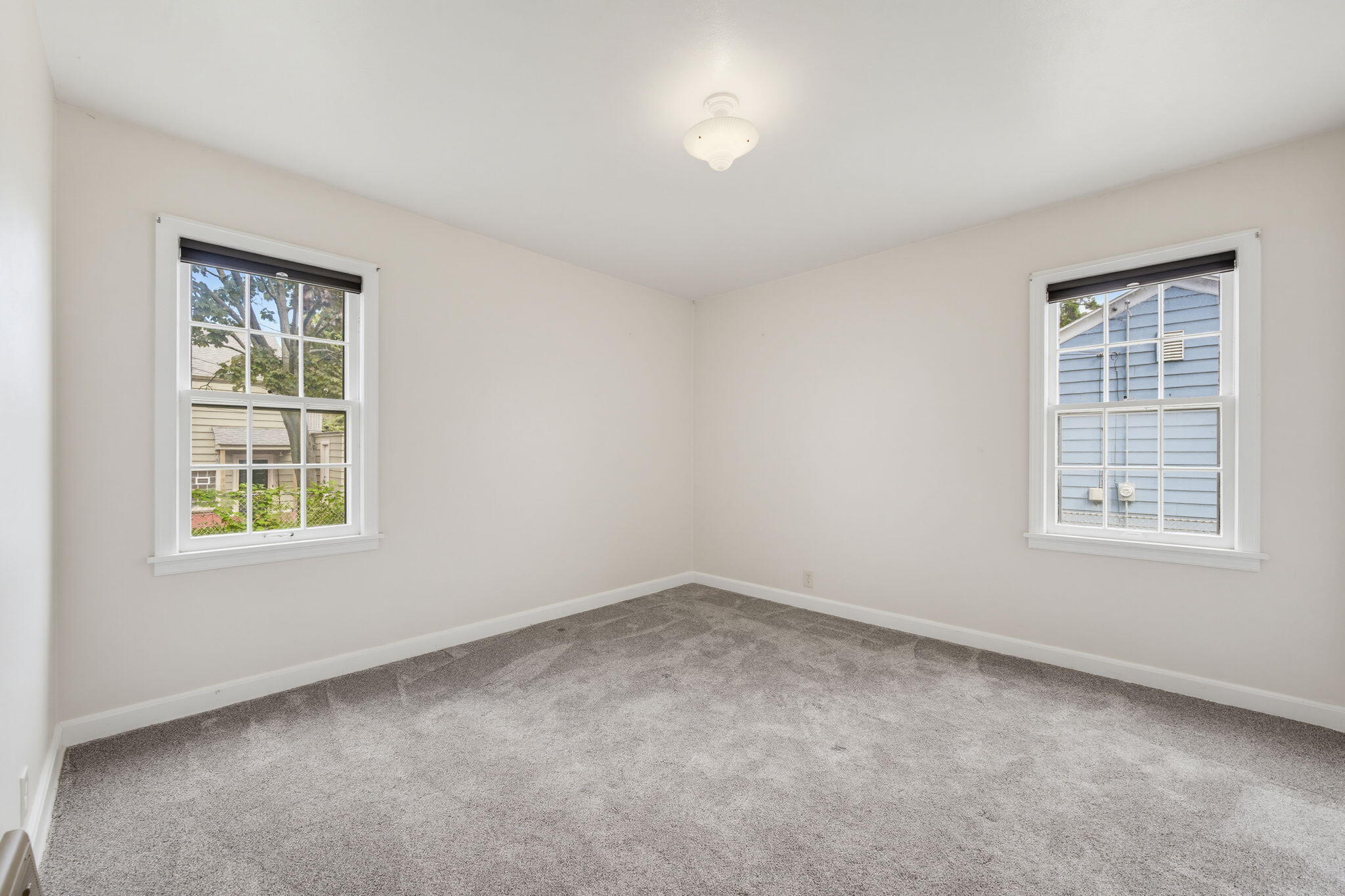 Empty bedroom with gray carpet, two windows, and a ceiling light.
