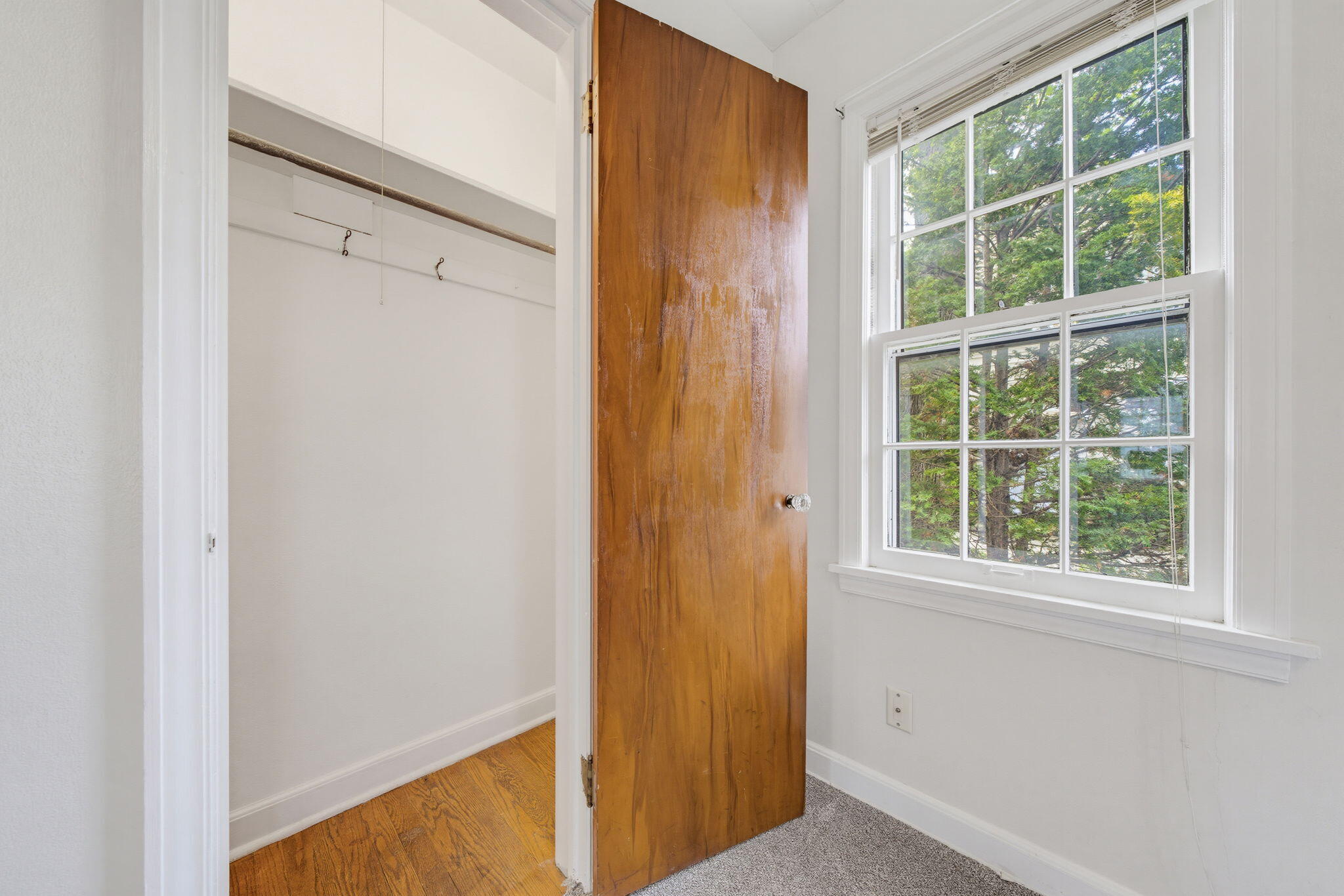 Unfurnished room with a large window and an open closet beside a wooden door.