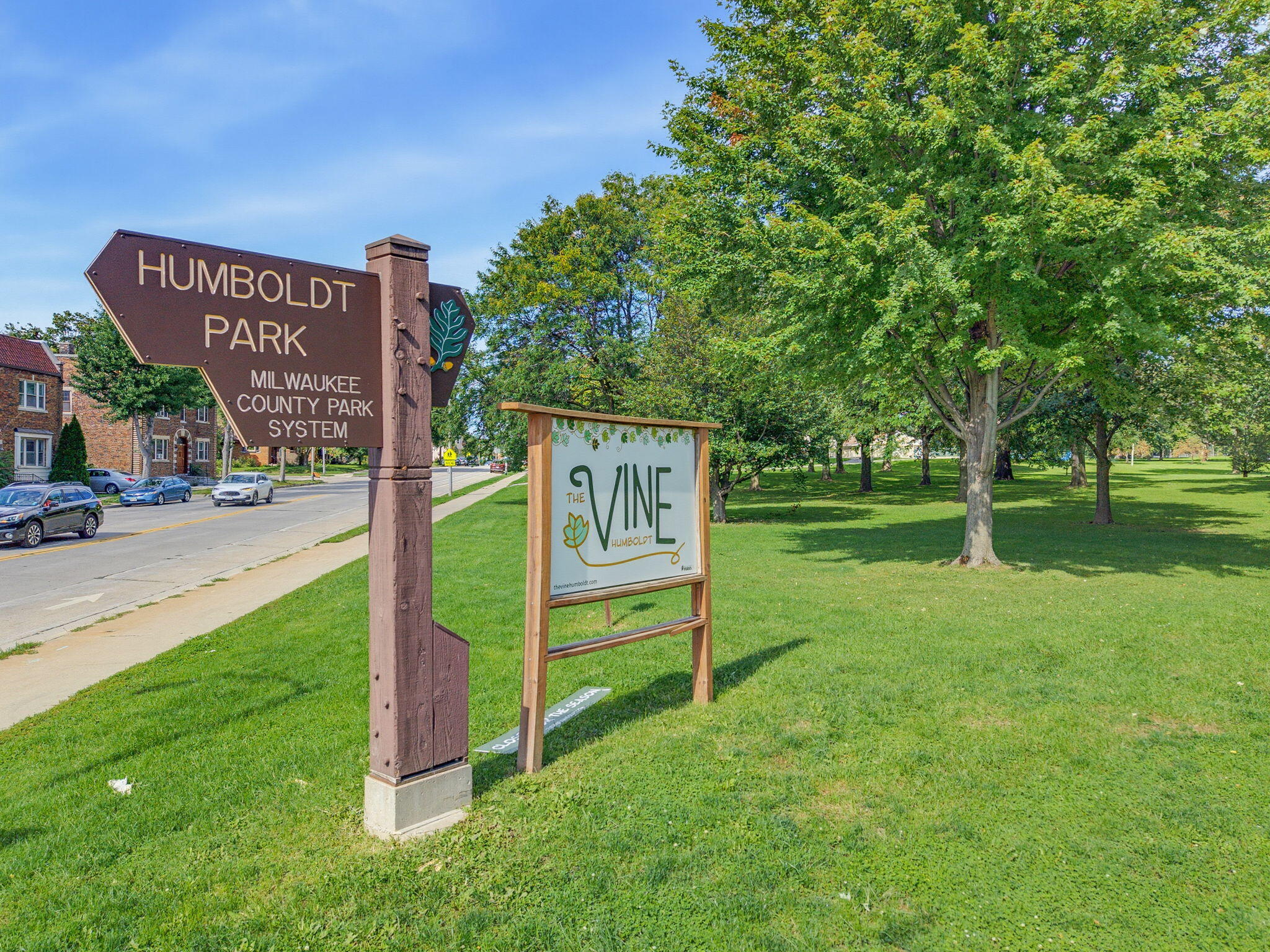 Humboldt Park entrance sign beside a tree-lined lawn and The Vine Humboldt sign.