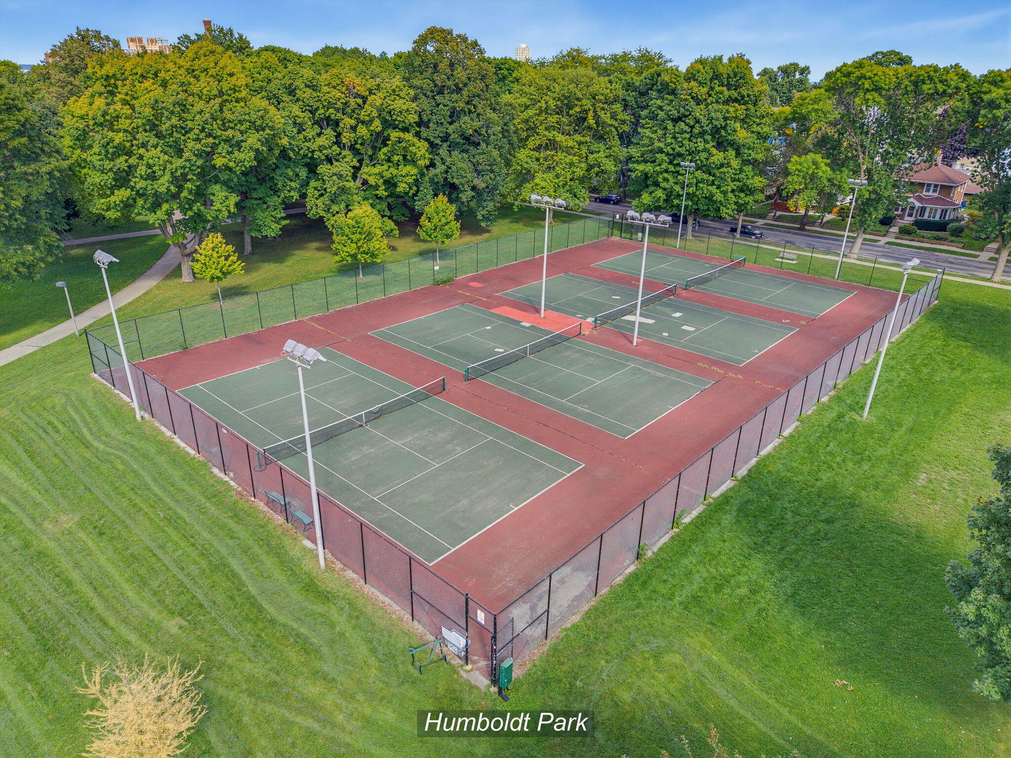 Aerial view of Humboldt Park tennis courts, with red surrounds, green playing surfaces, and mature trees.