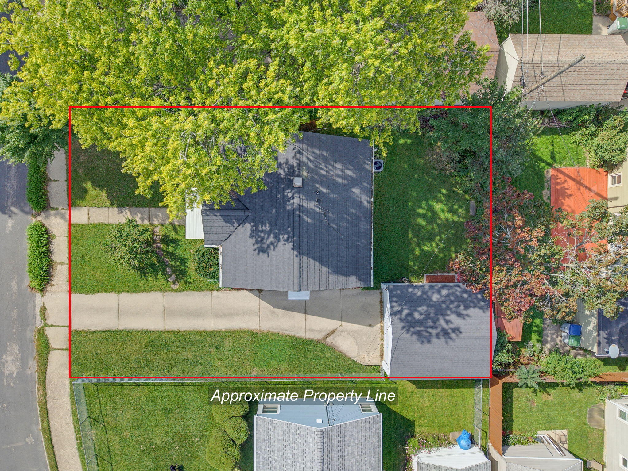 Aerial view of the house and lot outlined in red, with a lawn, mature trees, and curved driveway.
