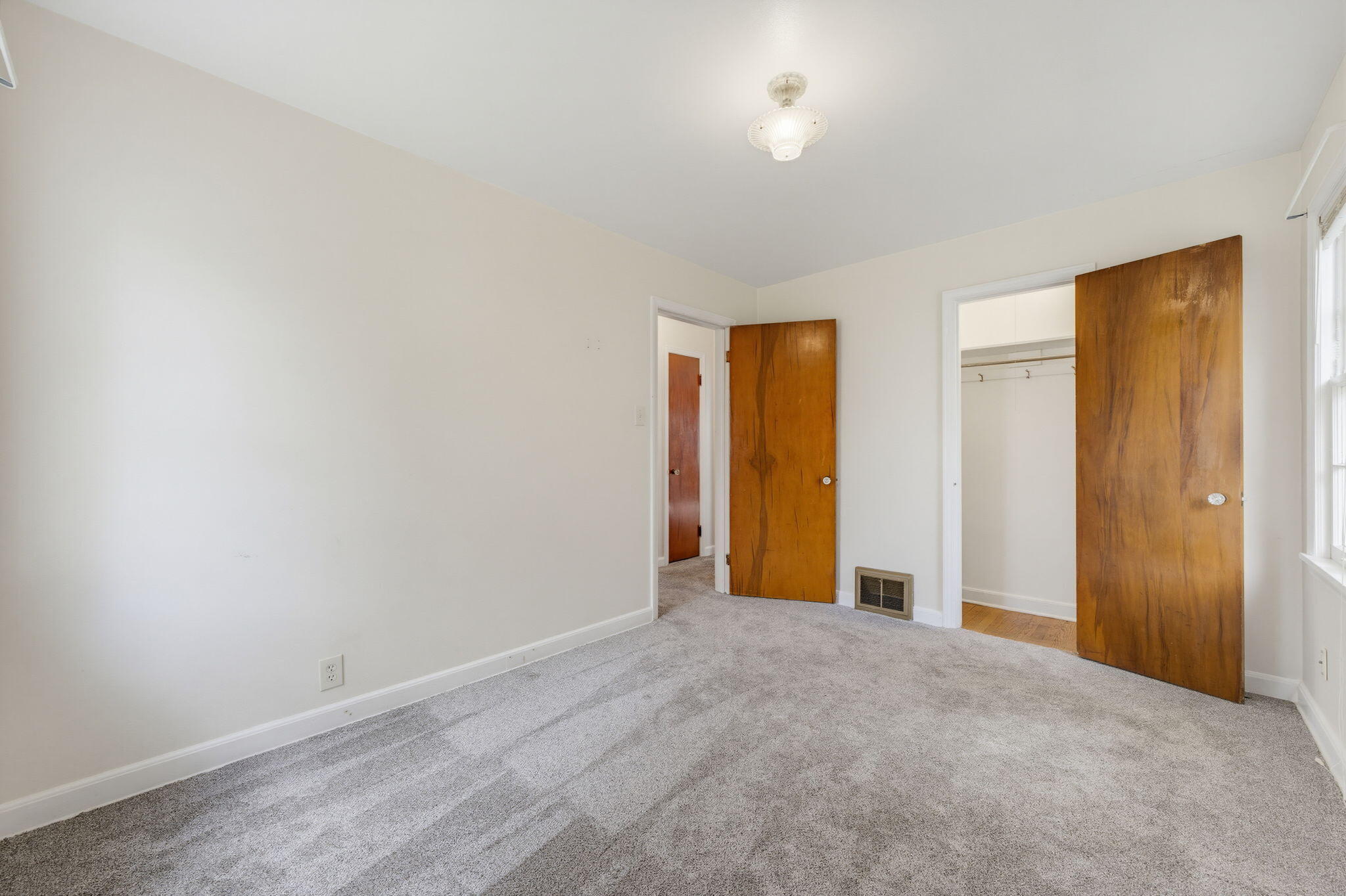 Empty bedroom with gray carpet, wooden doors, and a window.