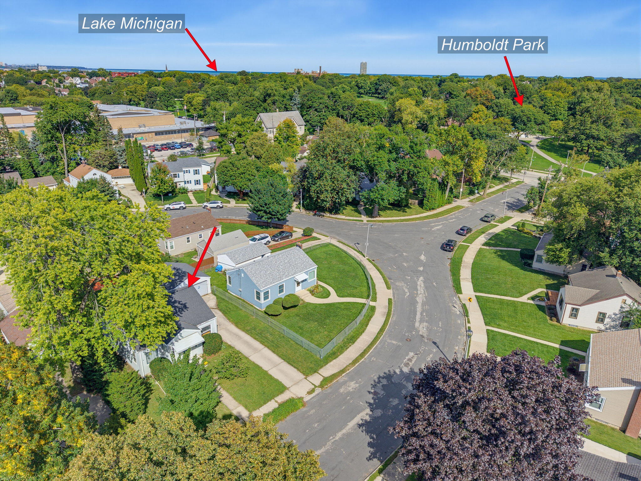 Aerial view of a light blue home on a curved street, with Lake Michigan and Humboldt Park in the distance.