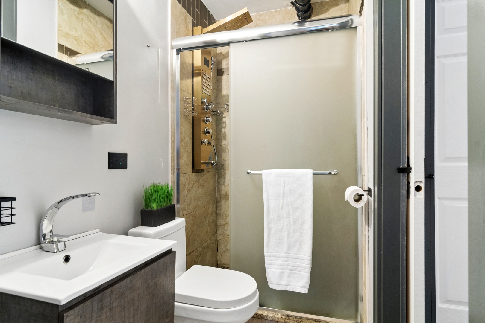 Modern bathroom with a dark vanity, white fixtures, and a frosted-glass shower with beige tile.