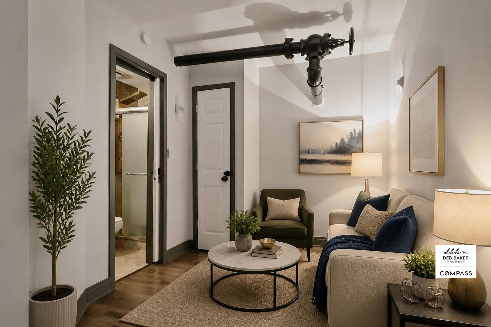 Staged living room with a cream sofa, round coffee table, and exposed black ceiling pipe.