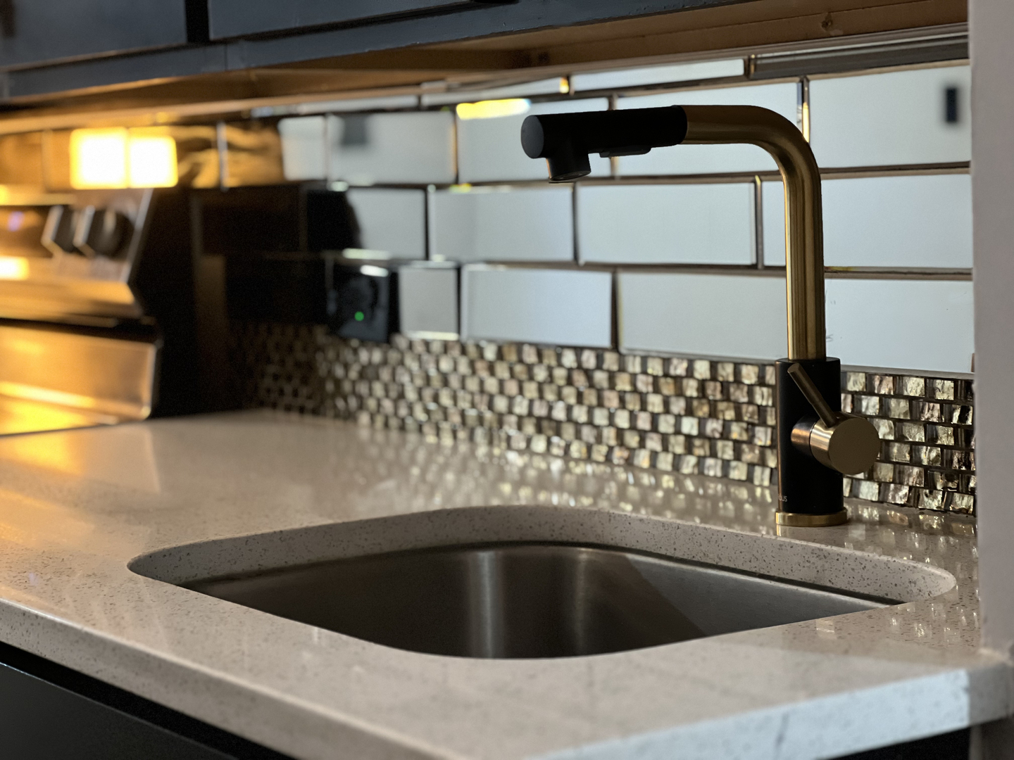 Kitchen sink with a brass-and-black faucet and mosaic backsplash
