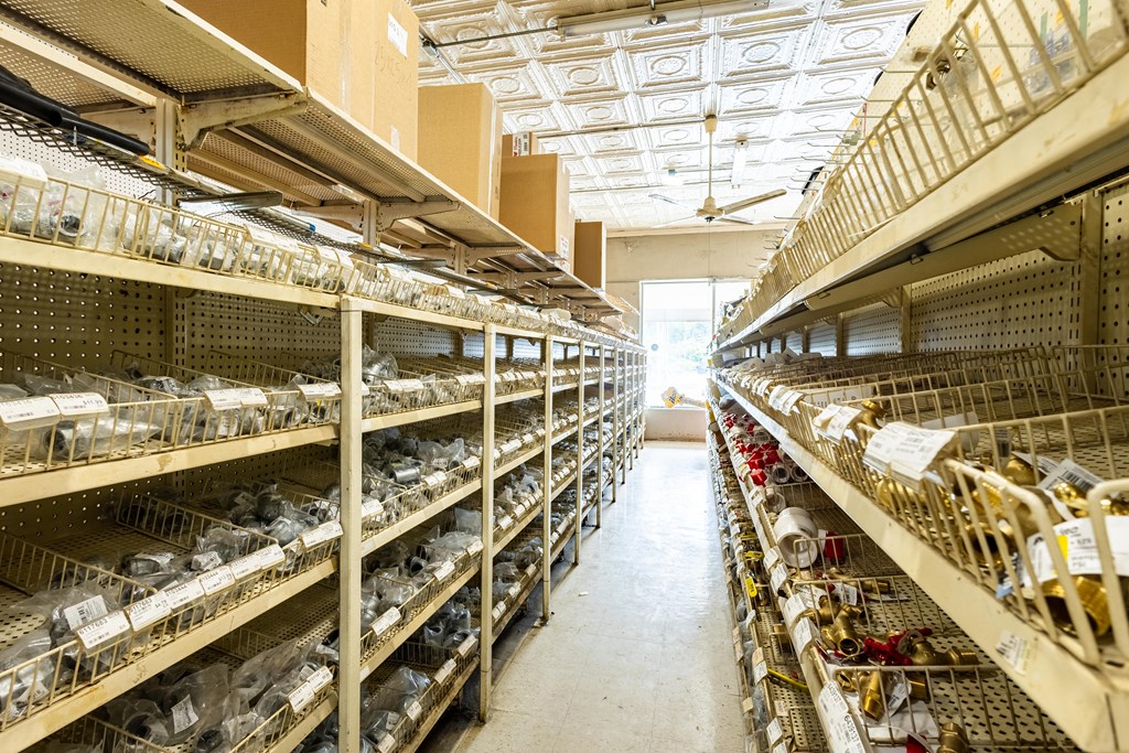 Retail supply store aisle lined with stocked shelves of plumbing and hardware parts.
