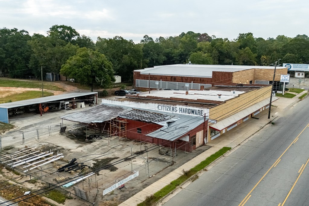 Citizens Hardware storefront with weathered metal roofs and a fenced materials yard beside the road.