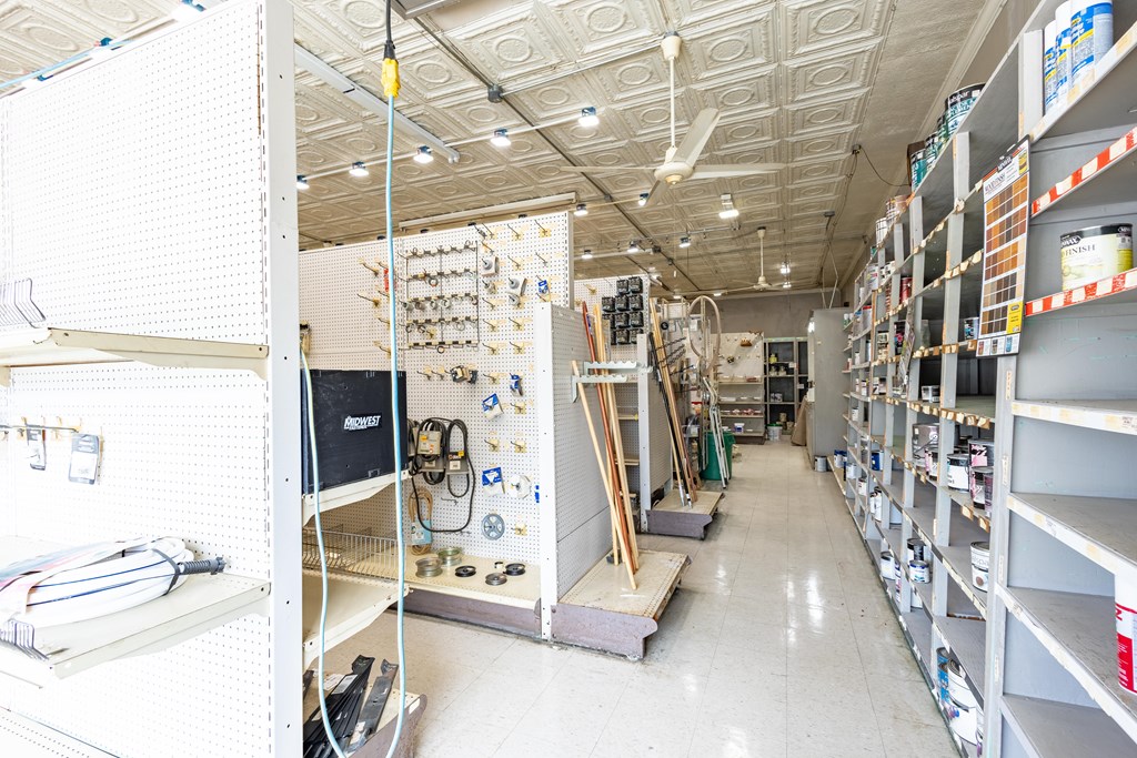 Retail shop aisle with shelves of building supplies and tools beneath a patterned tin ceiling.