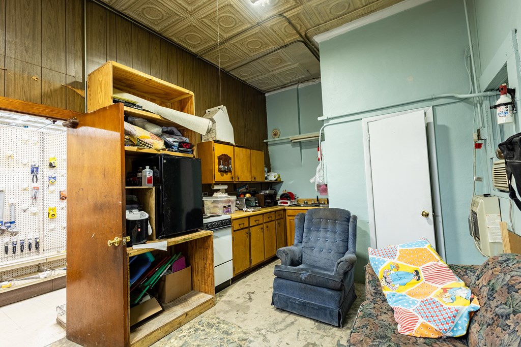 Crowded kitchen and sitting area with wooden cabinets, open shelving, and a patterned tin ceiling.