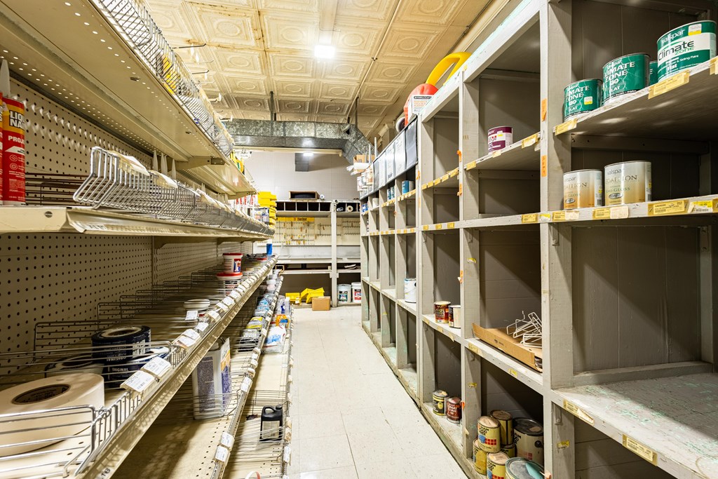 Supply-store aisle with paint cans and hardware shelves beneath a patterned ceiling.