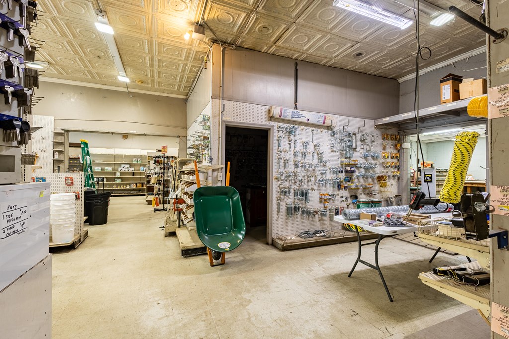 Hardware store interior with pegboard displays, a green wheelbarrow, and a patterned tin ceiling.
