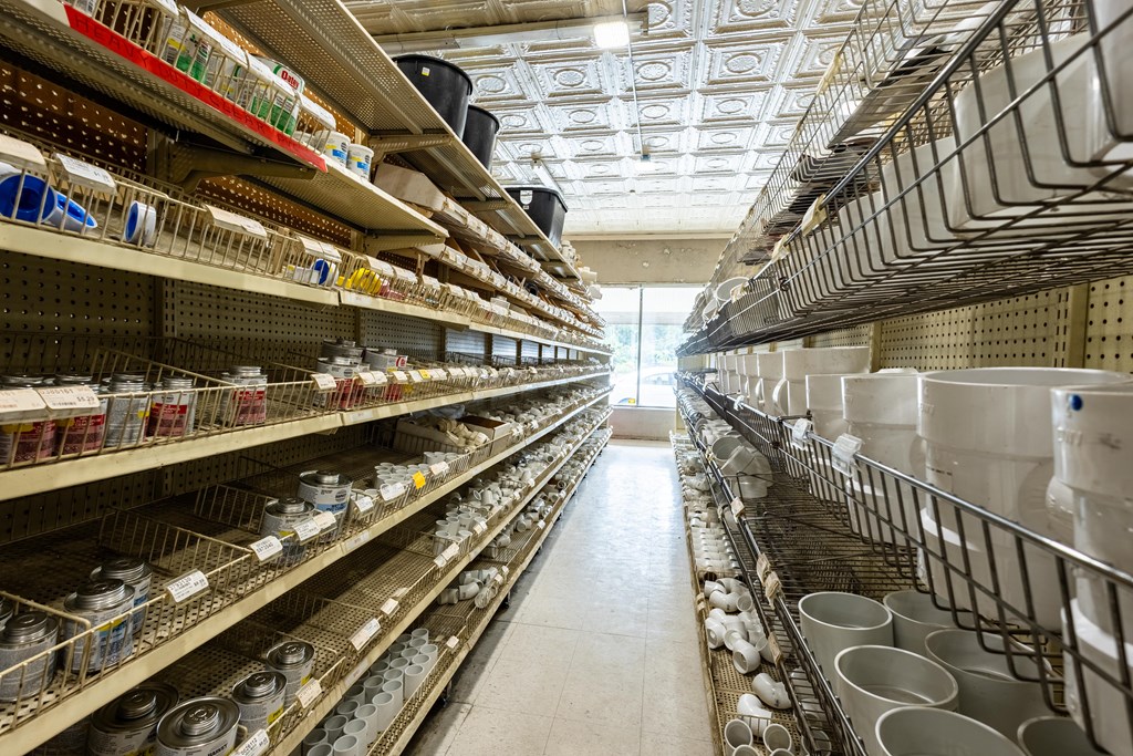 Store aisle lined with plumbing supplies and white sinks beneath a decorative tin ceiling.