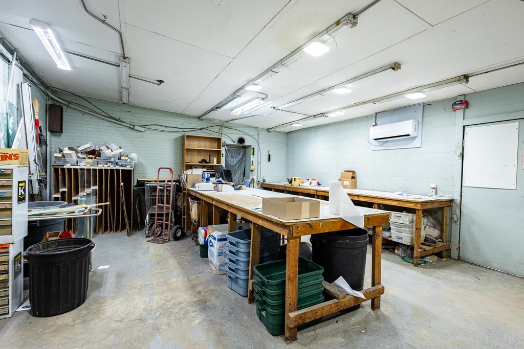 Workshop with long wooden worktables, storage bins, and fluorescent ceiling lights.