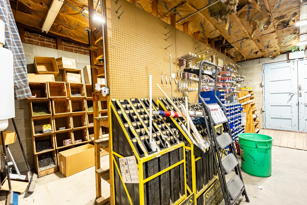 Workshop storage area with cubbies, tool racks, ladders, and exposed ceiling insulation.
