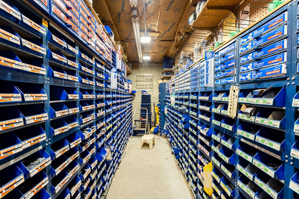 Hardware storage aisle with blue shelves packed with labeled bins of bolts and screws.