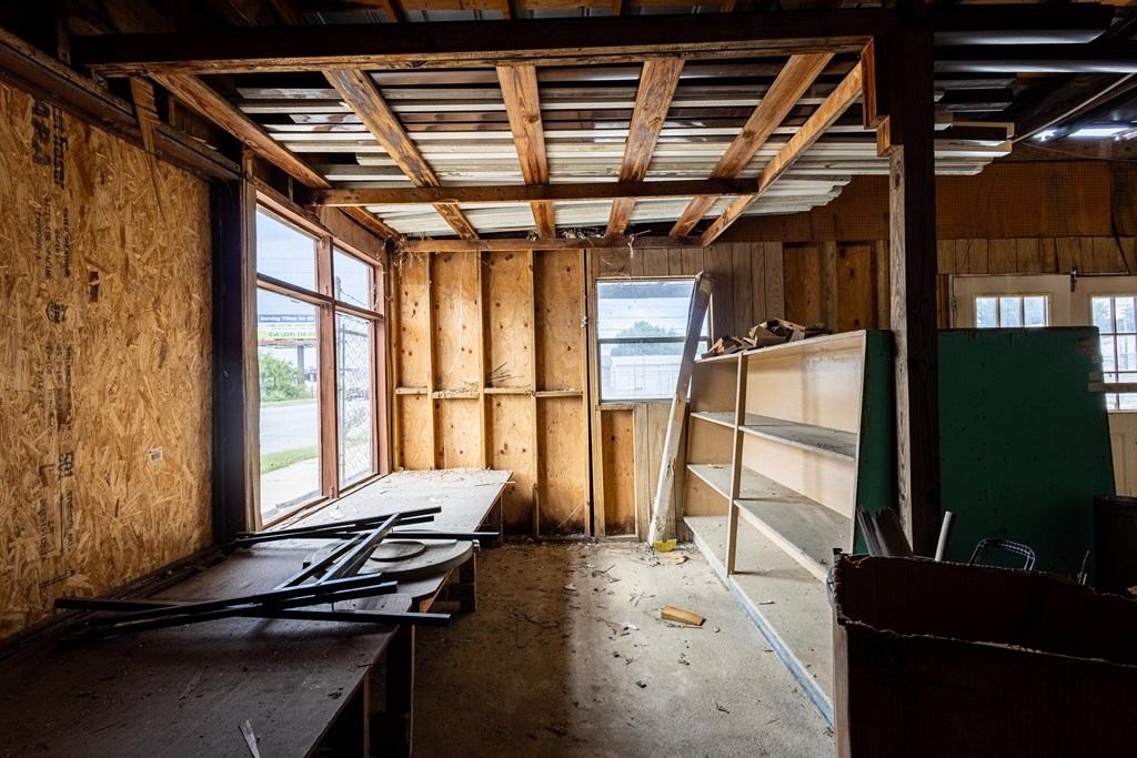 Unfinished interior with exposed wooden framing, dusty floor, debris, and empty shelving.