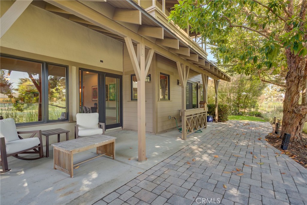 Covered patio with white seating, paver walkway, and mature shade tree.