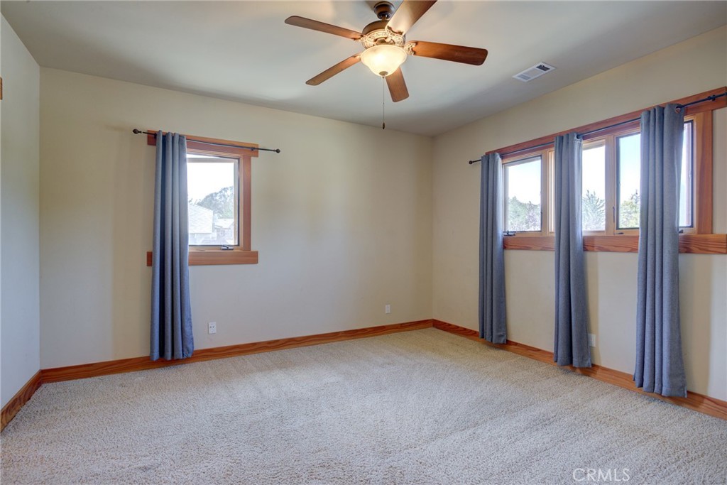 Empty carpeted bedroom with blue curtains, wood-trimmed windows, and a ceiling fan.