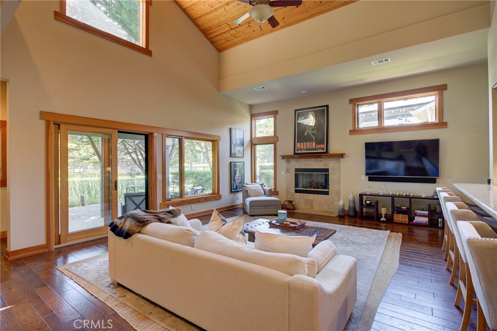 Living room with vaulted wood ceiling, stone fireplace, and large windows overlooking a patio.