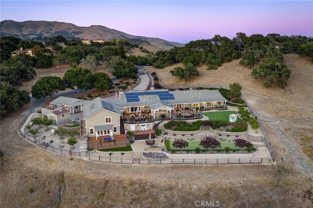 Aerial view of a ranch-style home with solar panels, landscaped grounds, and mountain views.