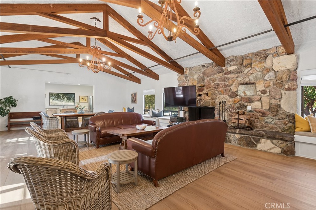 Living room with exposed wood beams, a stone fireplace, and leather seating beside an open dining area.