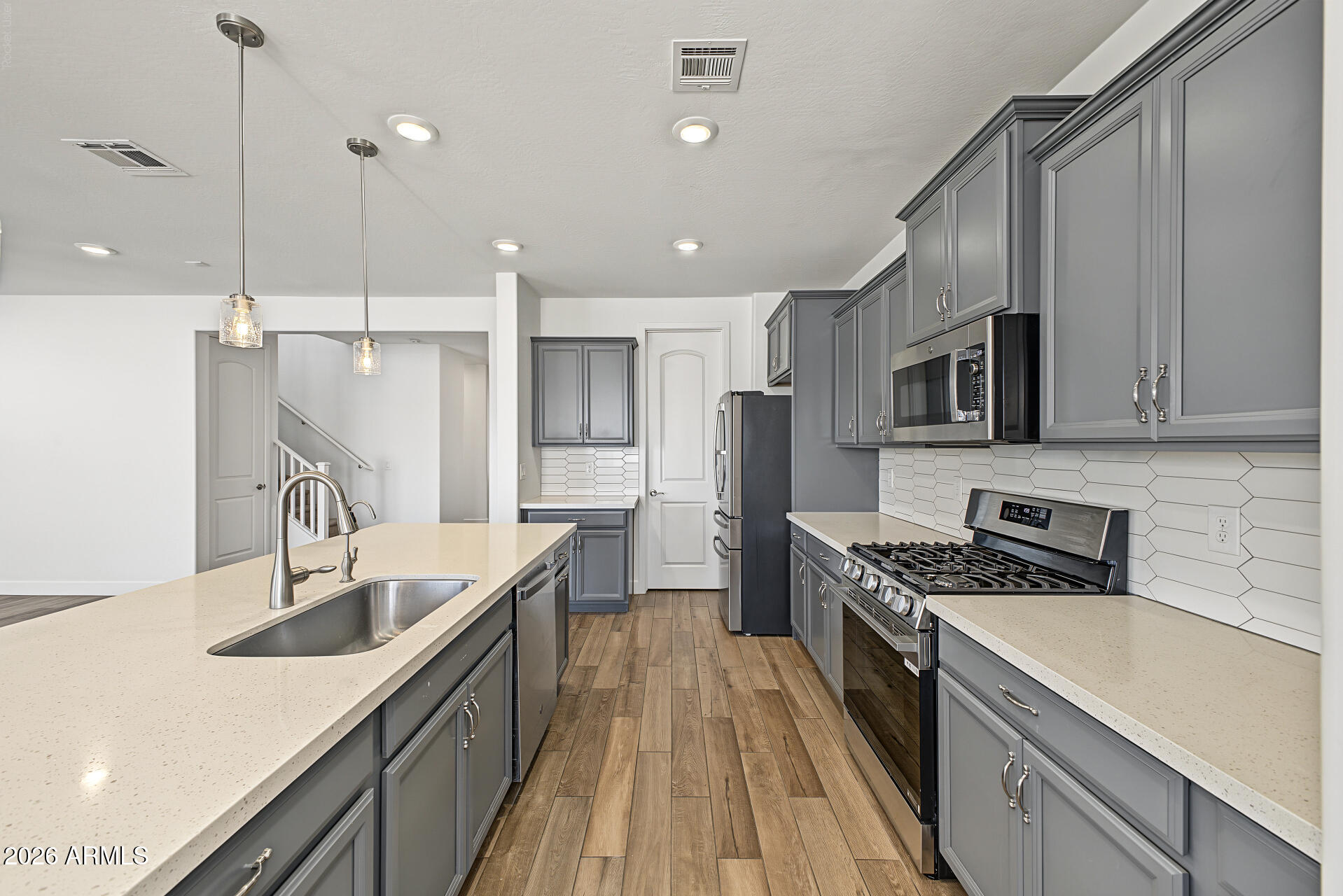 Modern kitchen with gray cabinets, white quartz island, stainless appliances, gas range, and geometric tile backsplash.