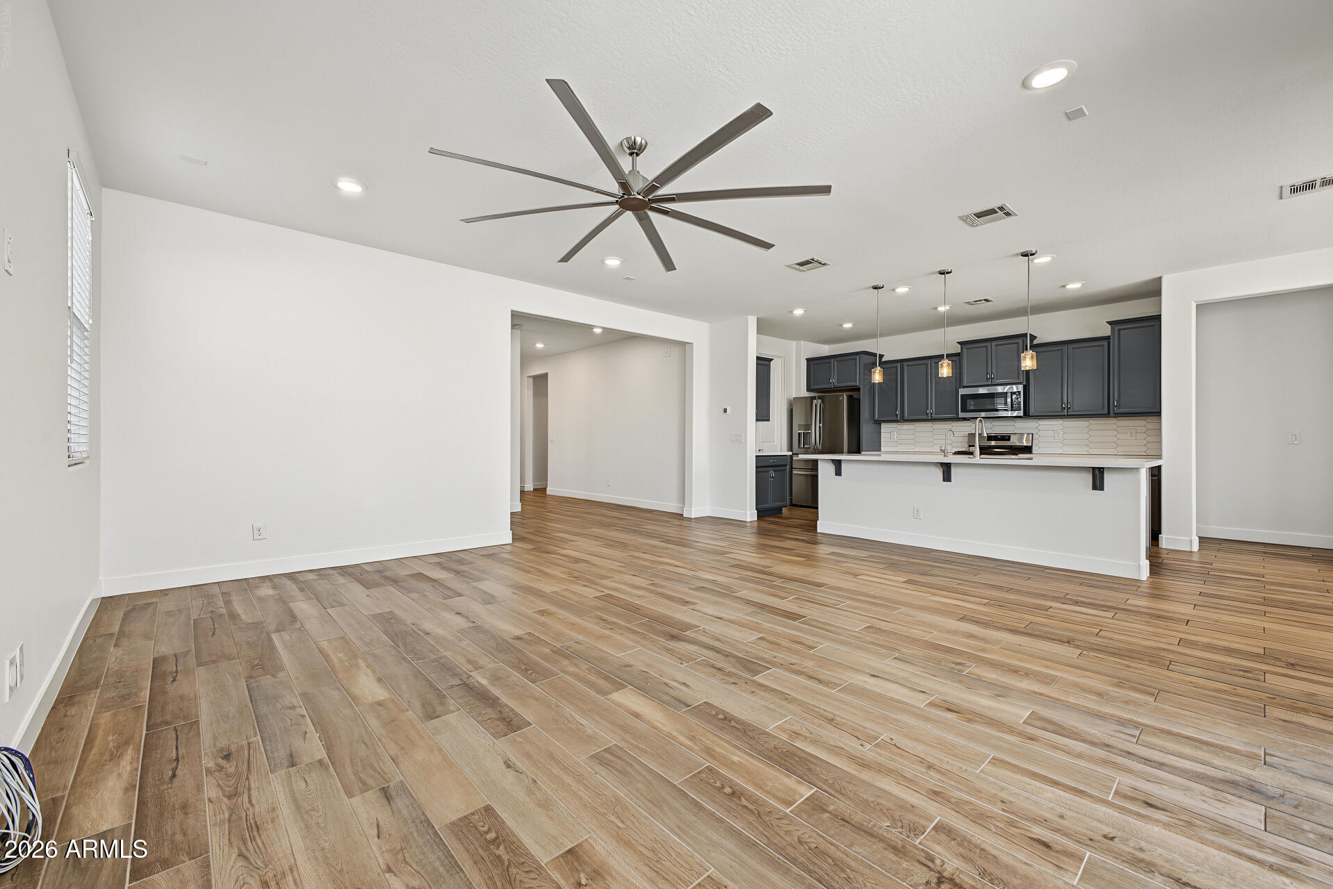 Open-plan living area with wood-look tile flooring, a large ceiling fan, and dark kitchen cabinets.