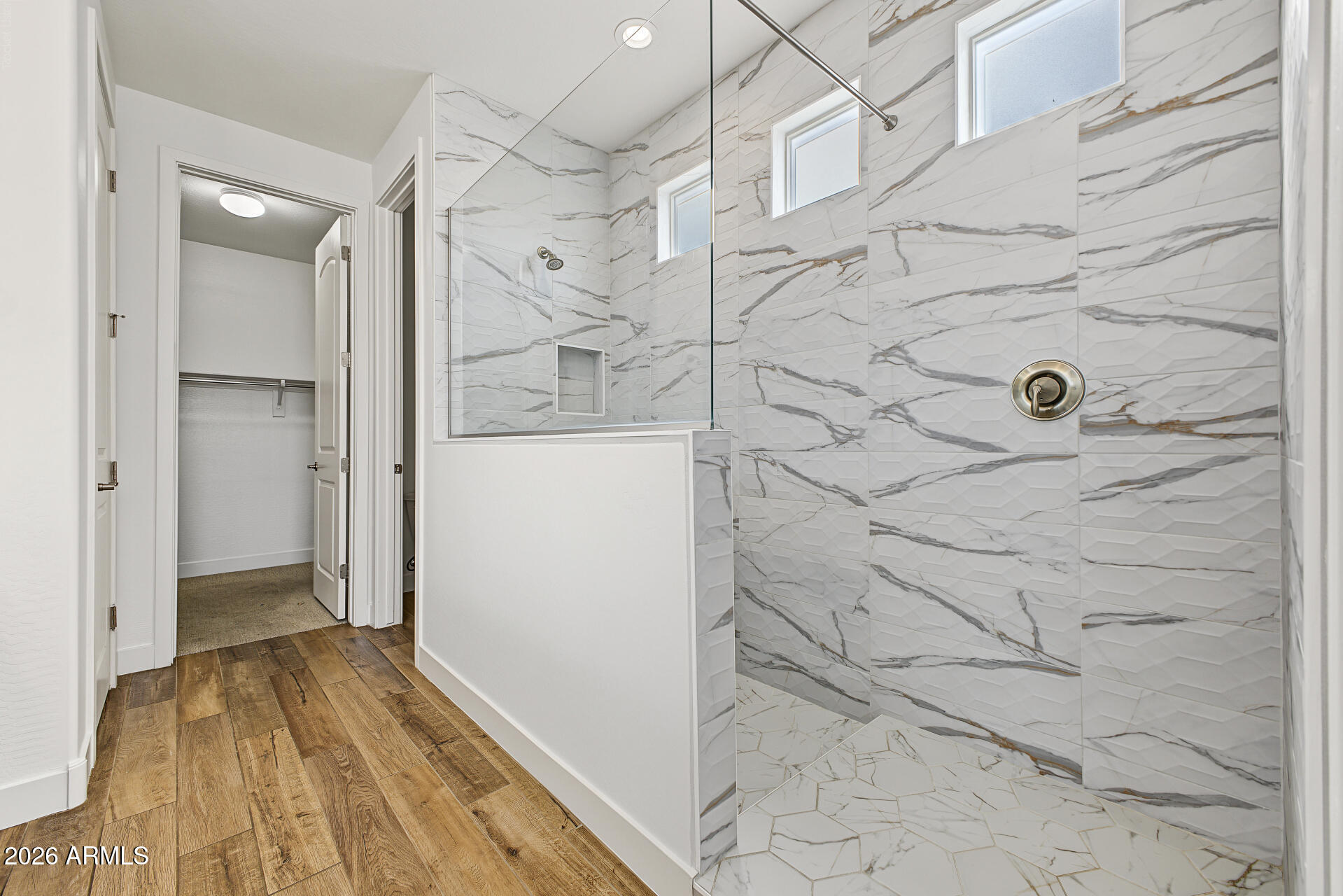 Bathroom with glass-enclosed walk-in shower, marble-pattern tile, and wood-look flooring.