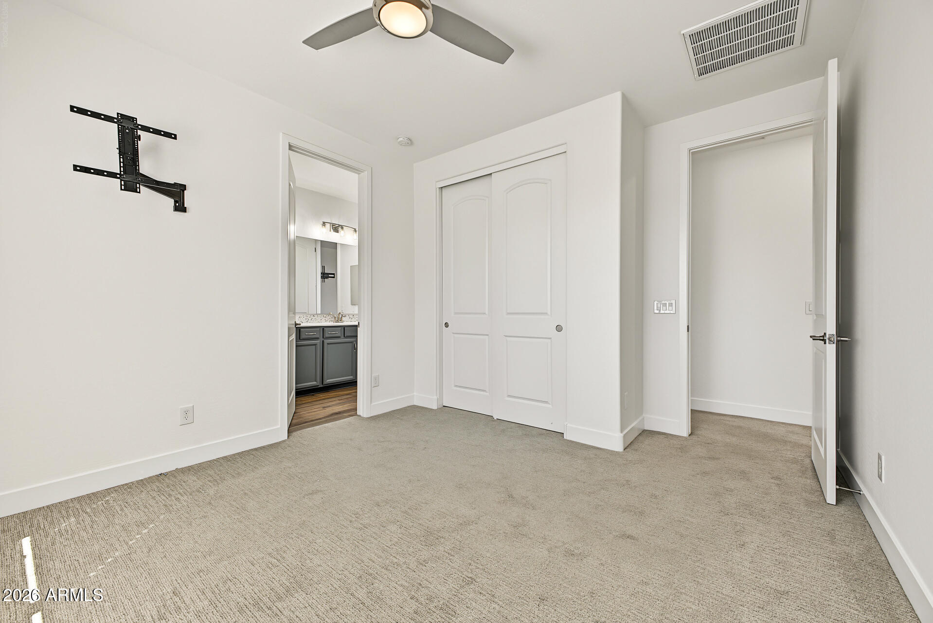 Empty carpeted bedroom with a ceiling fan, TV mount, and sliding closet doors.