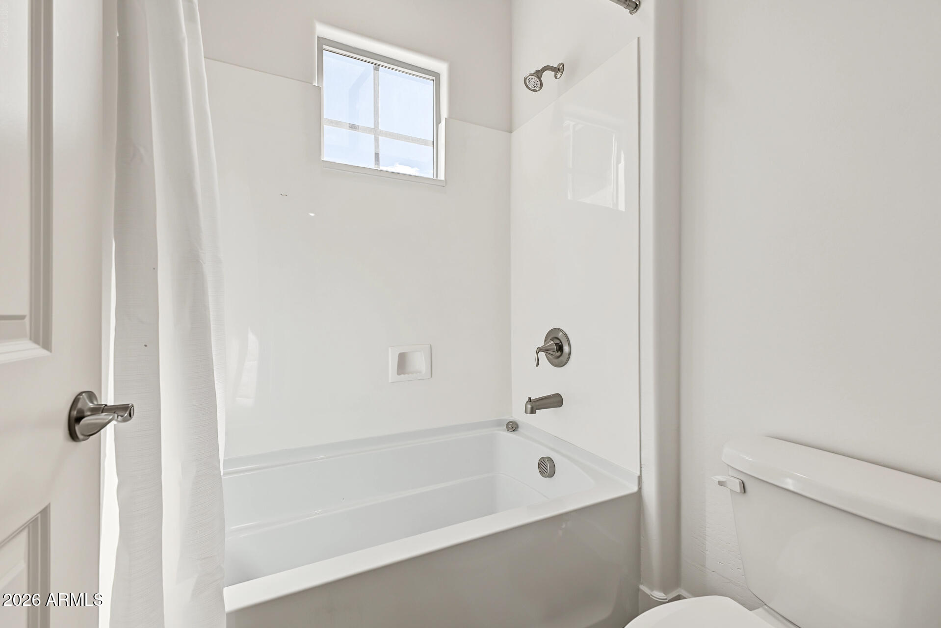 White bathtub and shower with a high window and toilet.