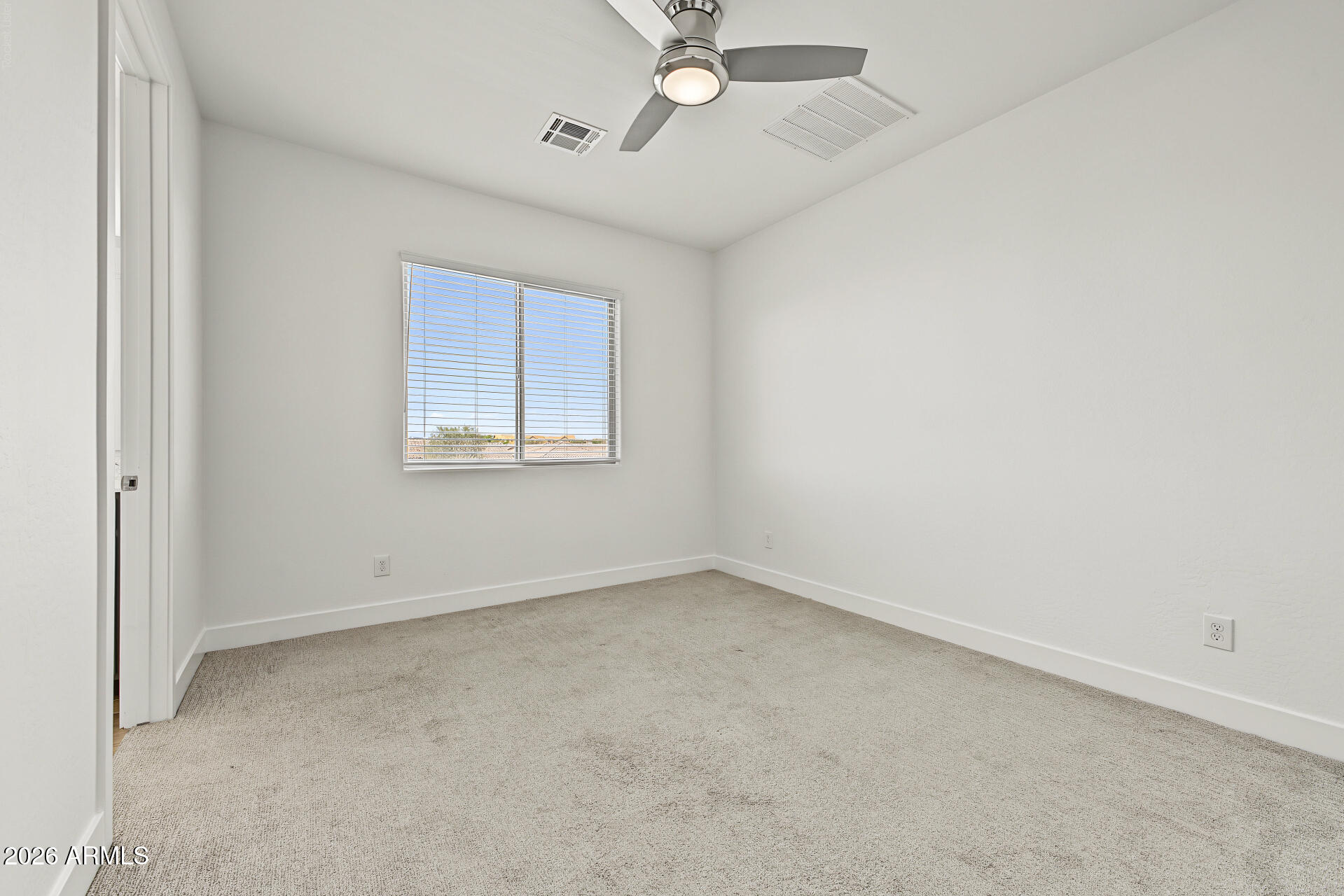 Empty carpeted room with white walls, window blinds, and a ceiling fan with light.