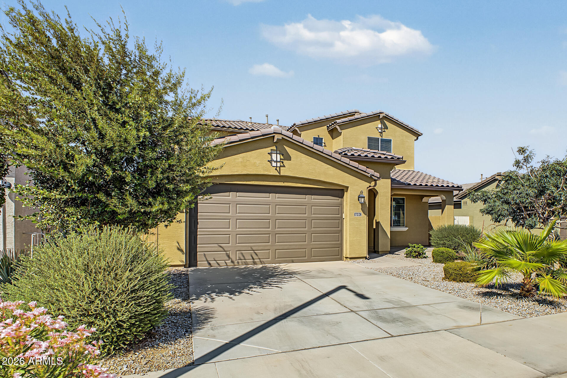 Two-story yellow stucco home with a tile roof, double garage, and desert landscaping.