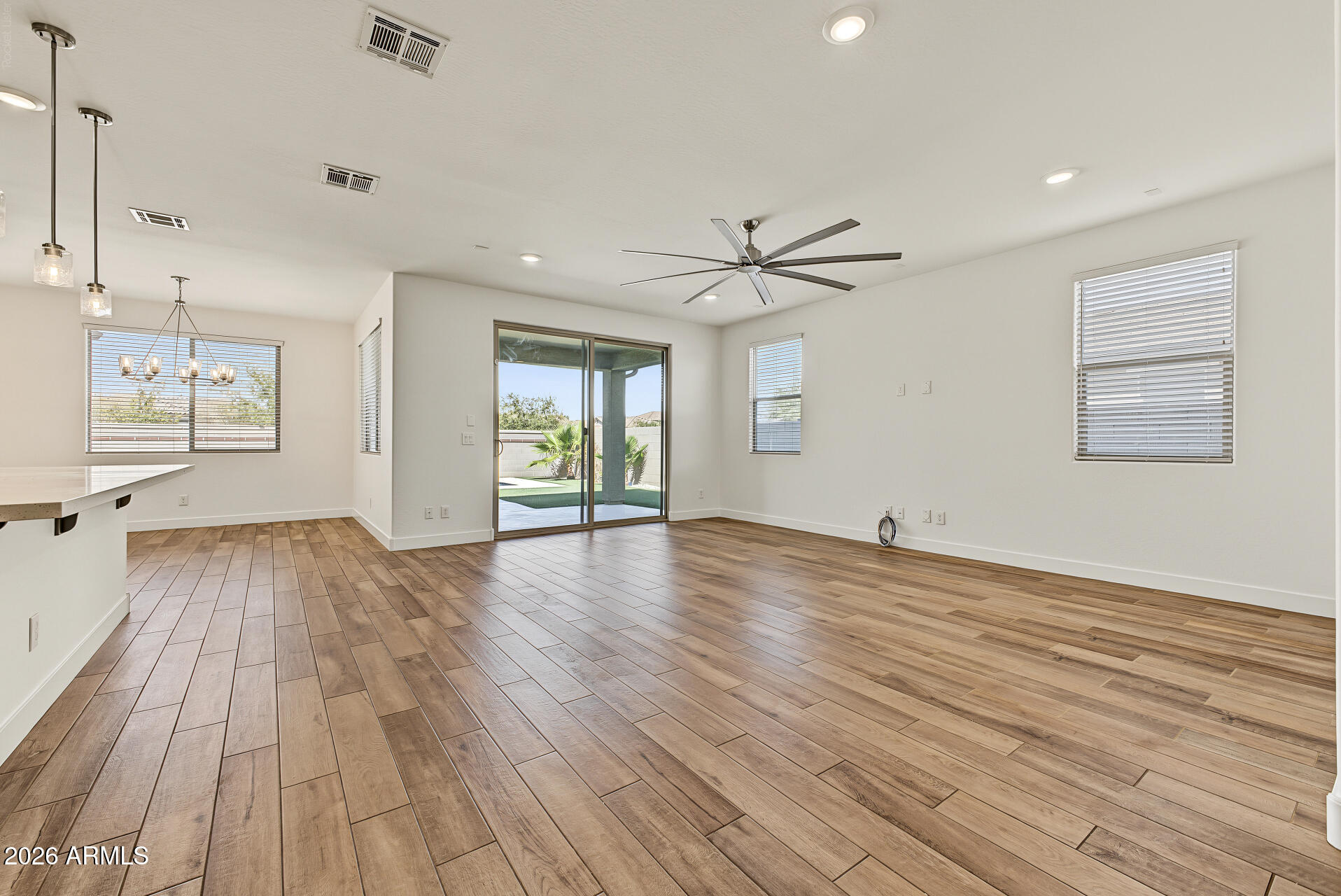 Empty open living and dining area with wood-look tile floors and sliding glass doors to a covered patio.