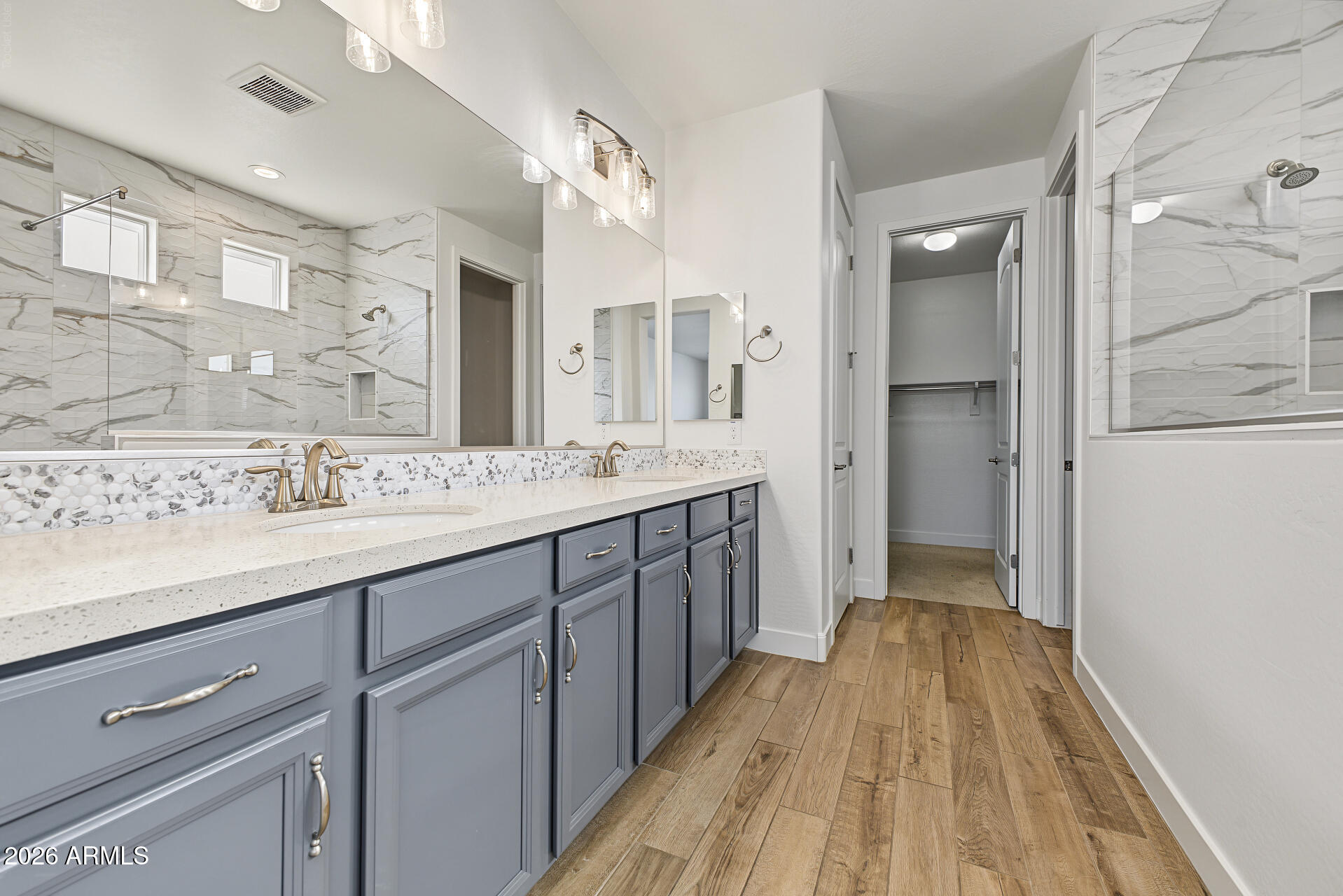 Bathroom with a double vanity, gray cabinets, marble-look tile, and wood-look flooring.