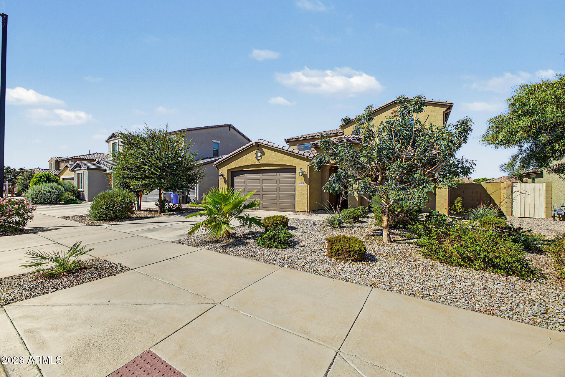 Tan stucco home with a two-car garage, wide driveway, and desert landscaping.