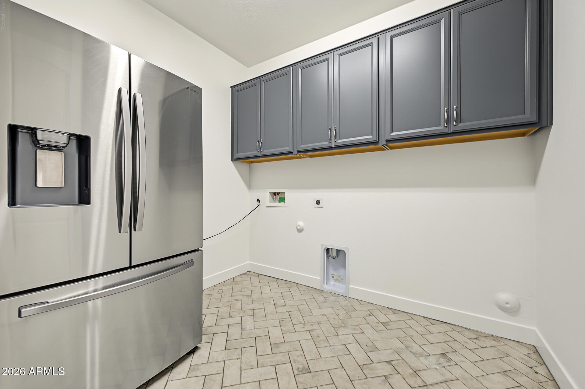 Laundry room with a stainless refrigerator, dark gray cabinets, and patterned tile floor.