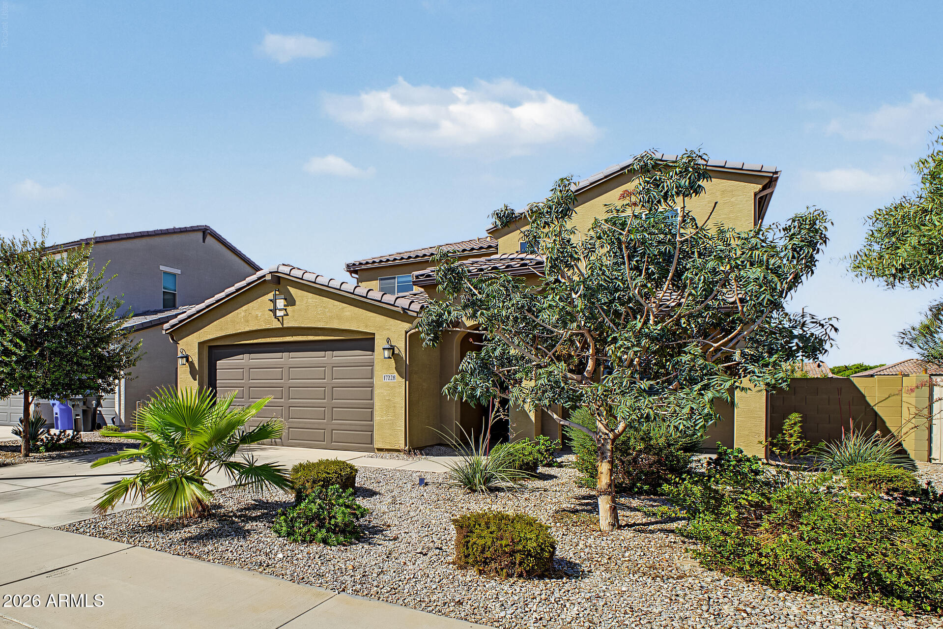 Tan two-story stucco home with a double garage, tiled roof, and desert landscaping.