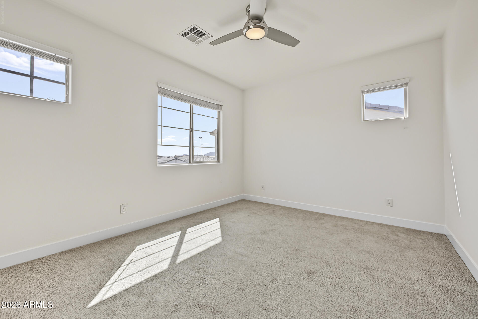 Empty bedroom with beige carpet, three windows, and a ceiling fan.