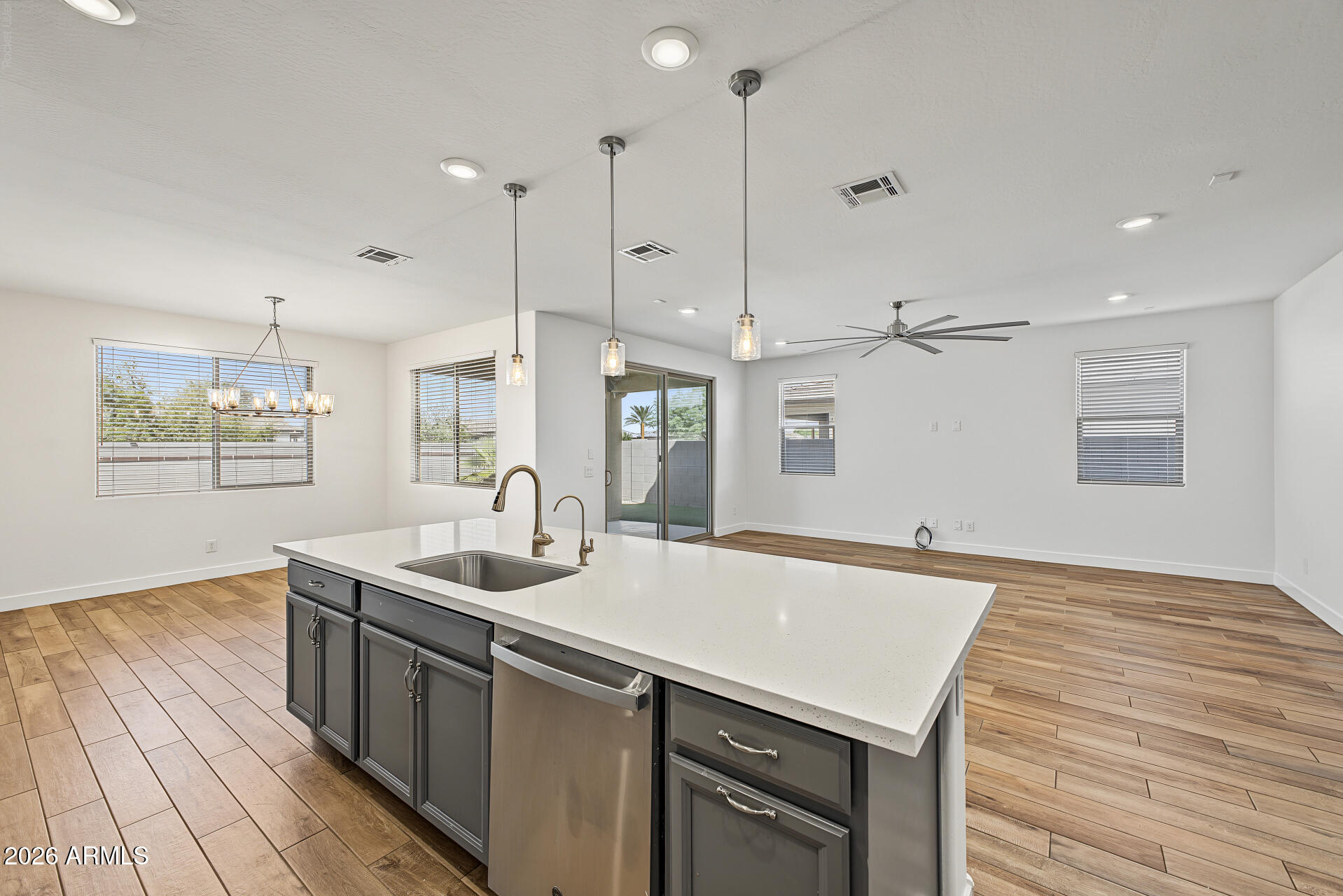 Open-plan kitchen with a large island, pendant lights, wood-look floors, and sliding glass doors.