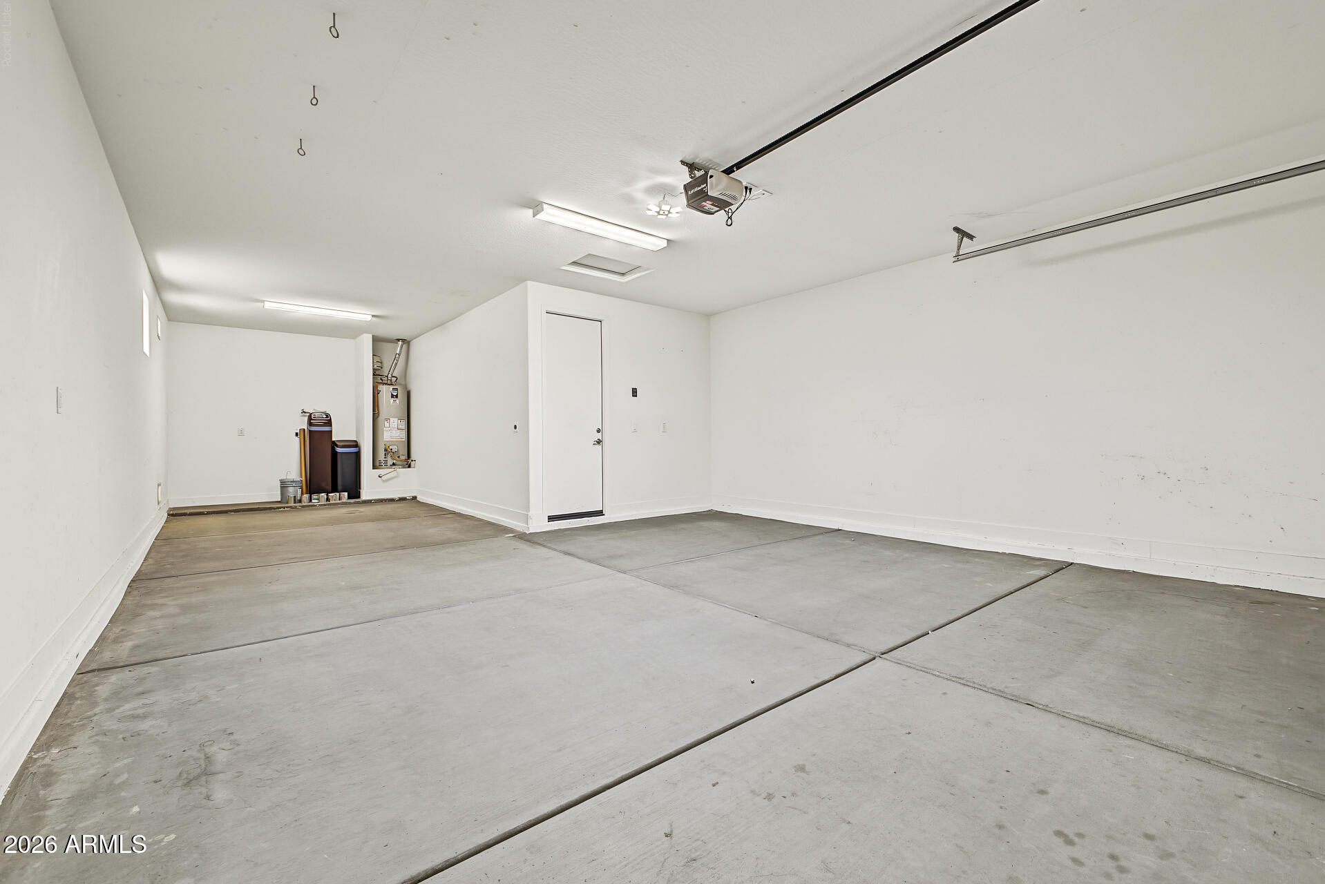 Empty garage with a wide concrete floor, ceiling-mounted opener, and utility equipment at the rear.