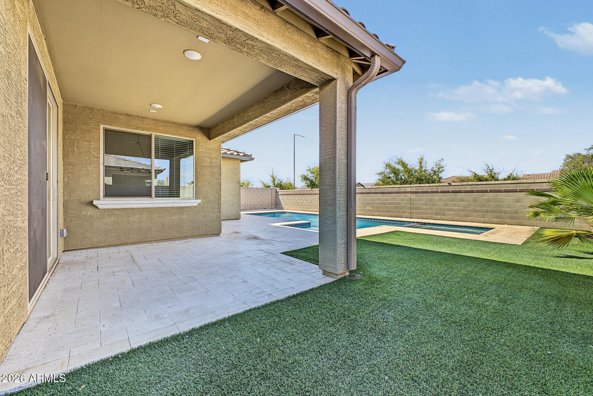 Backyard with a covered tiled patio, swimming pool, and artificial turf.
