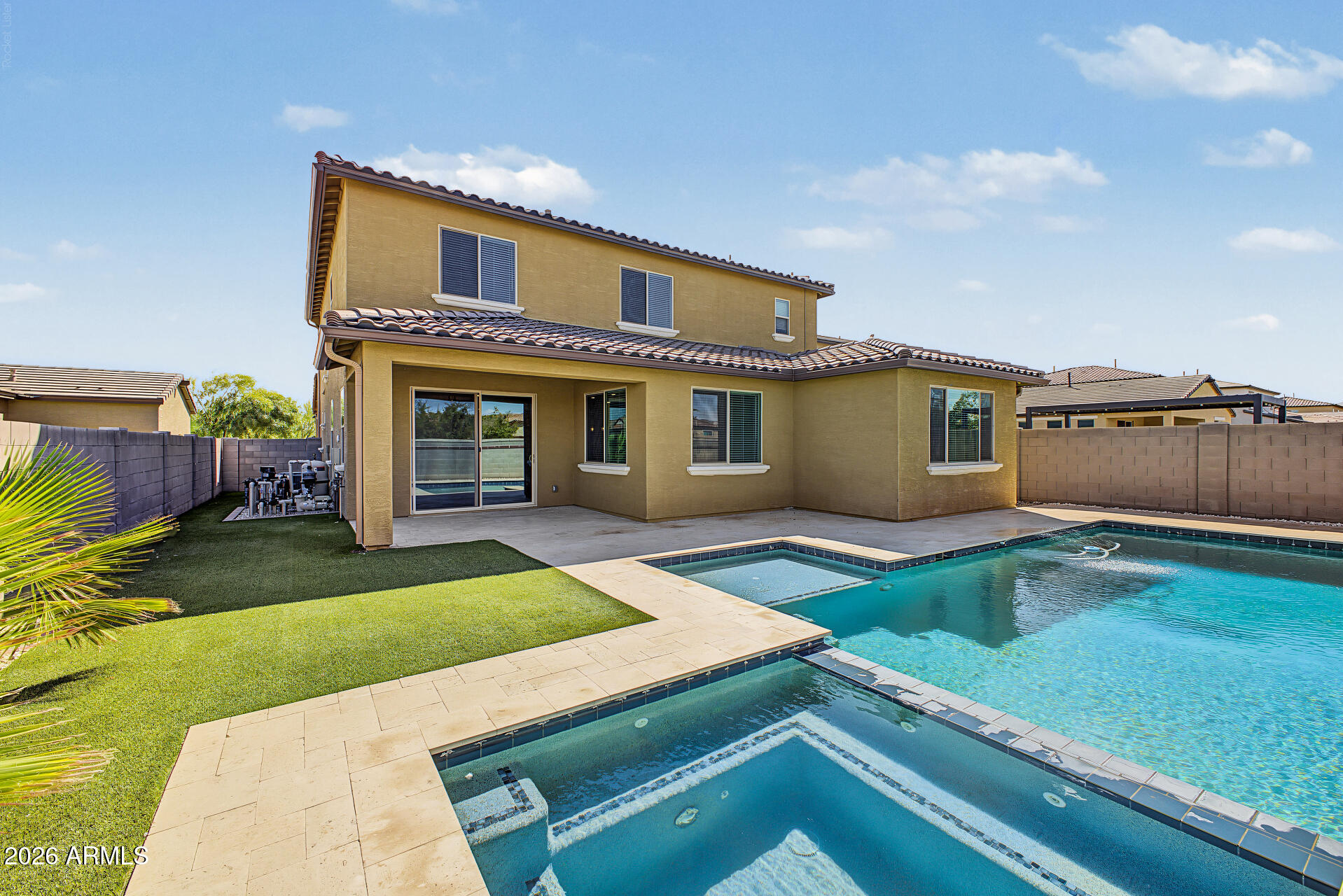 Two-story tan home behind a backyard pool, spa, paved patio, and artificial turf.