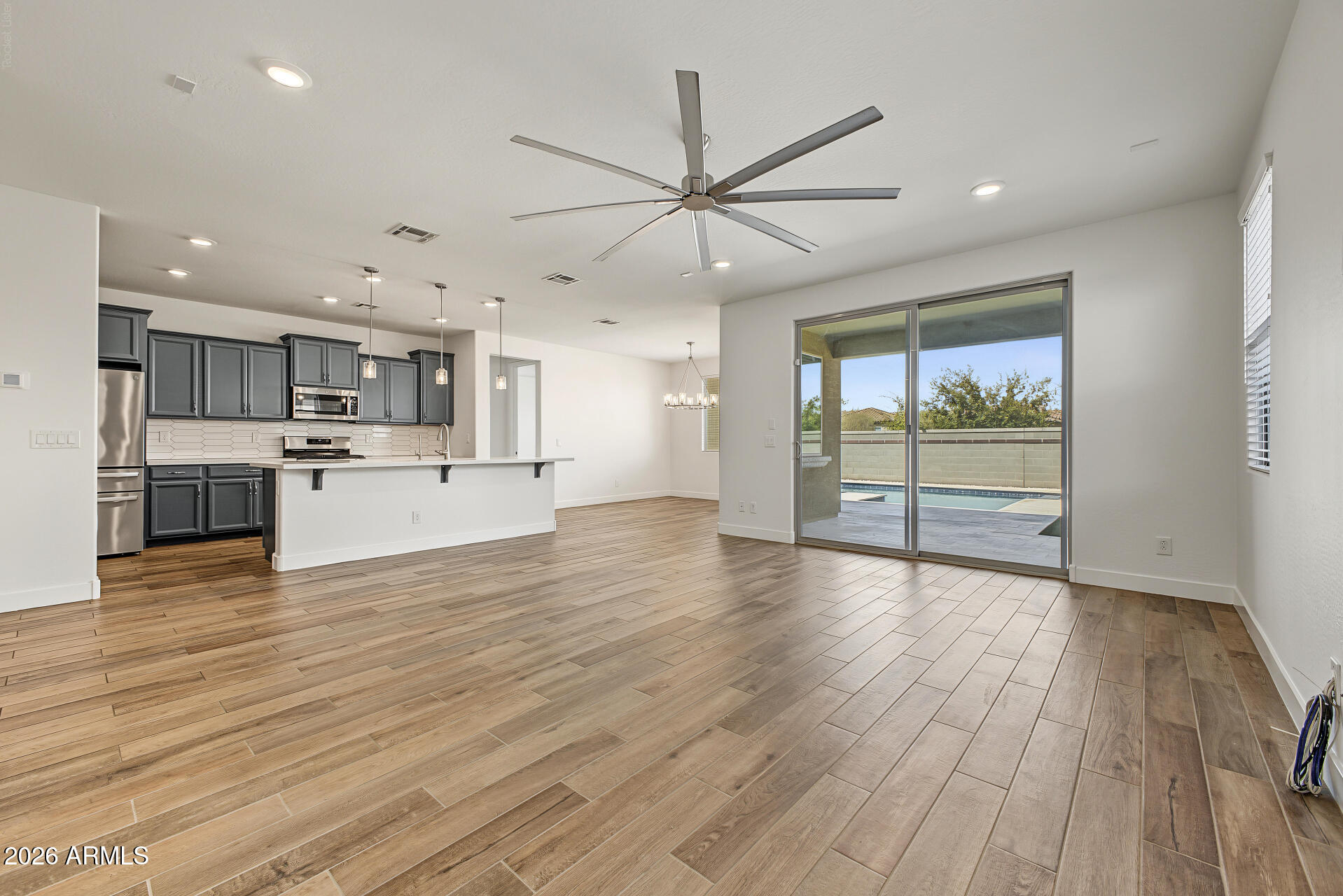 Open-plan kitchen and living area with gray cabinets, wood-look floors, and sliding doors to the pool.