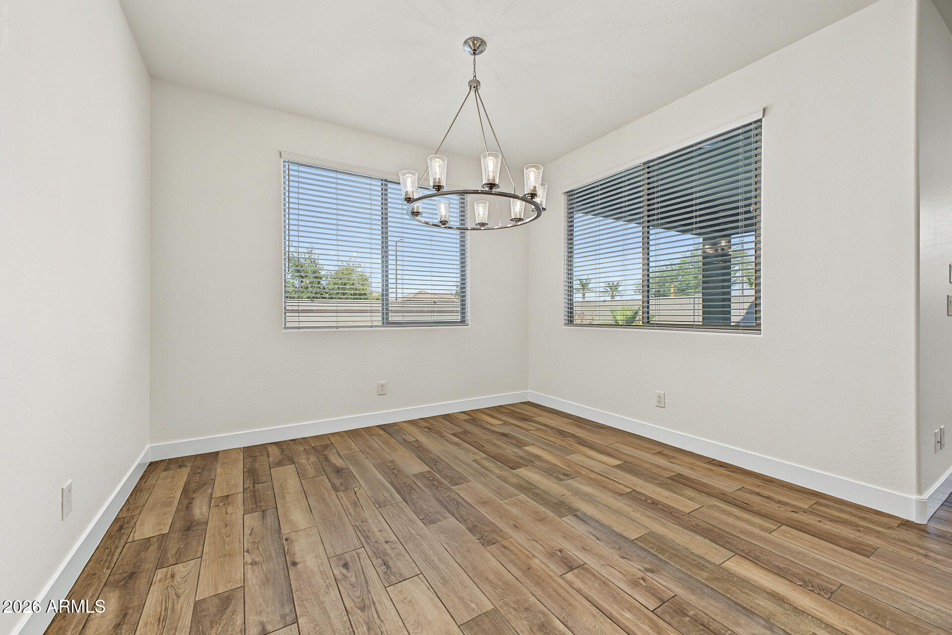 Empty dining room with wood-look flooring, two windows with blinds, and a circular chandelier.